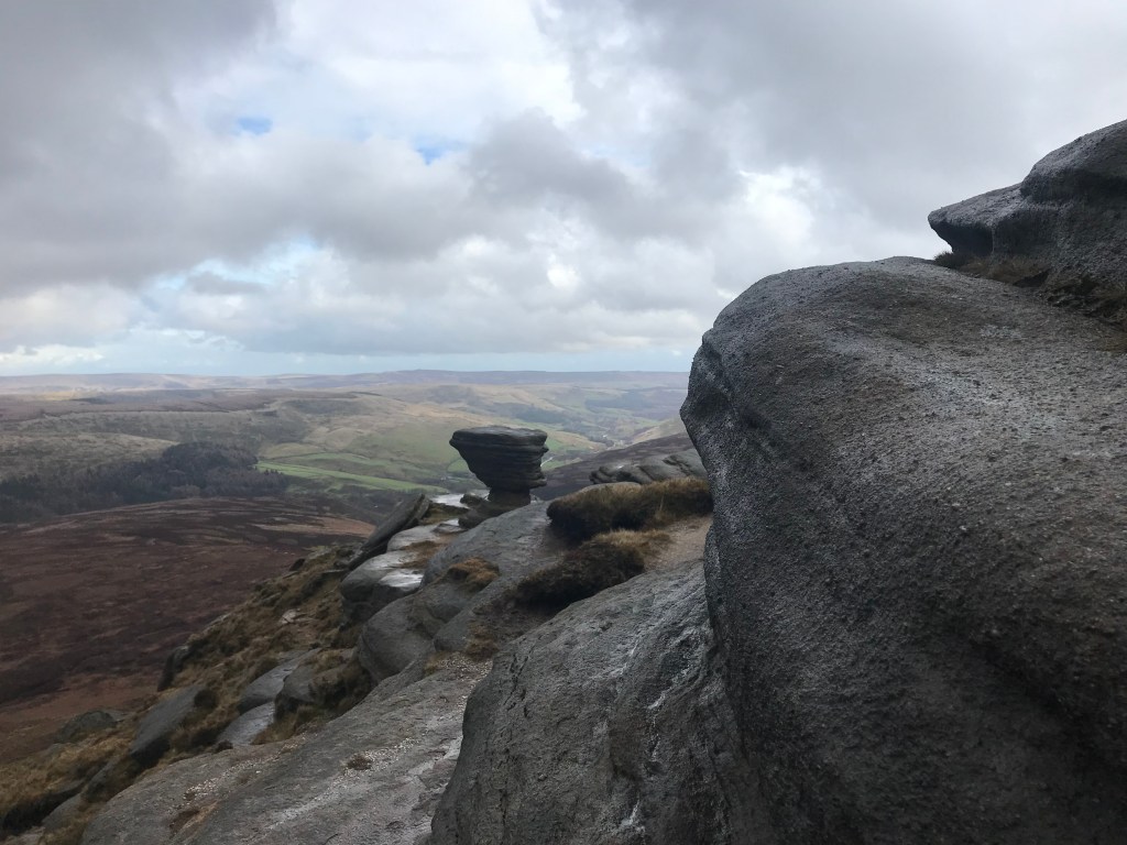 Steep, rounded rocks overlooking a heather-covered valley.  The sky is cloudy with hints of blue.