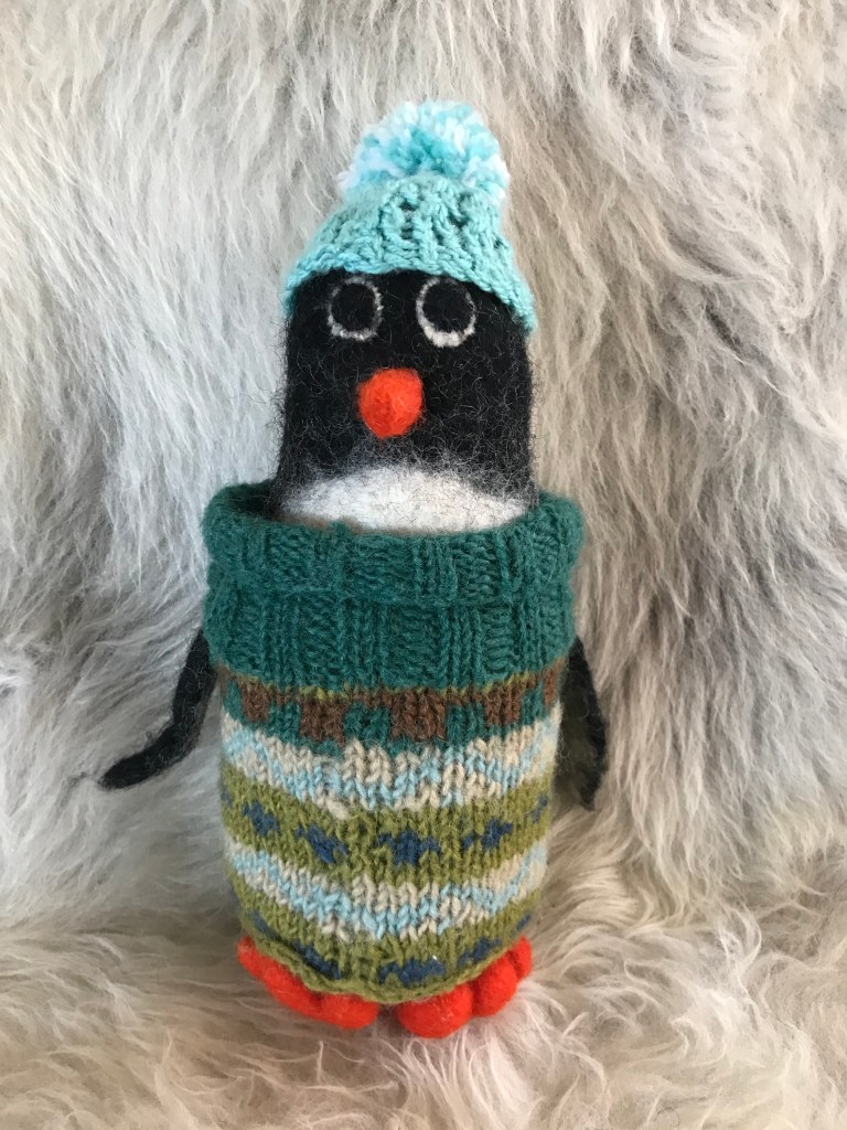 A felt penguin wearing a fair isle jumper and bobble hat