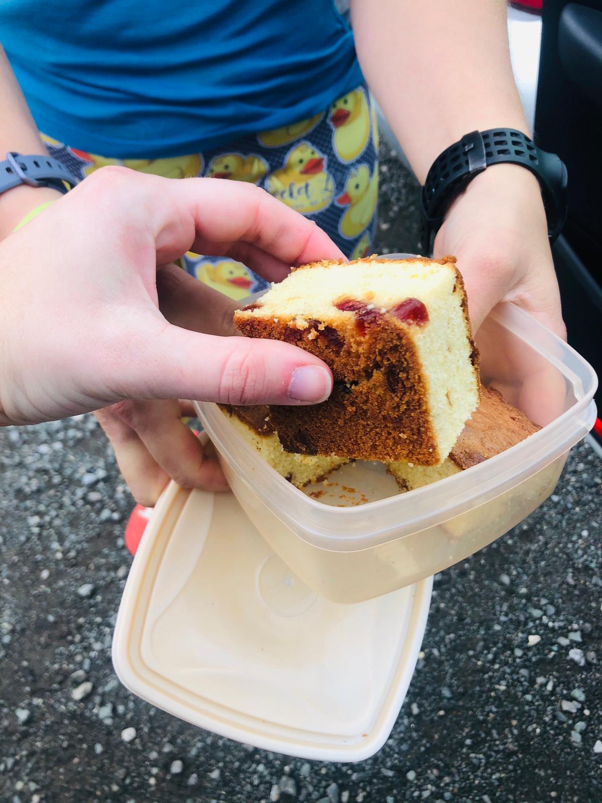 a hand taking cherry cake from a plastic tub, held out by another person.