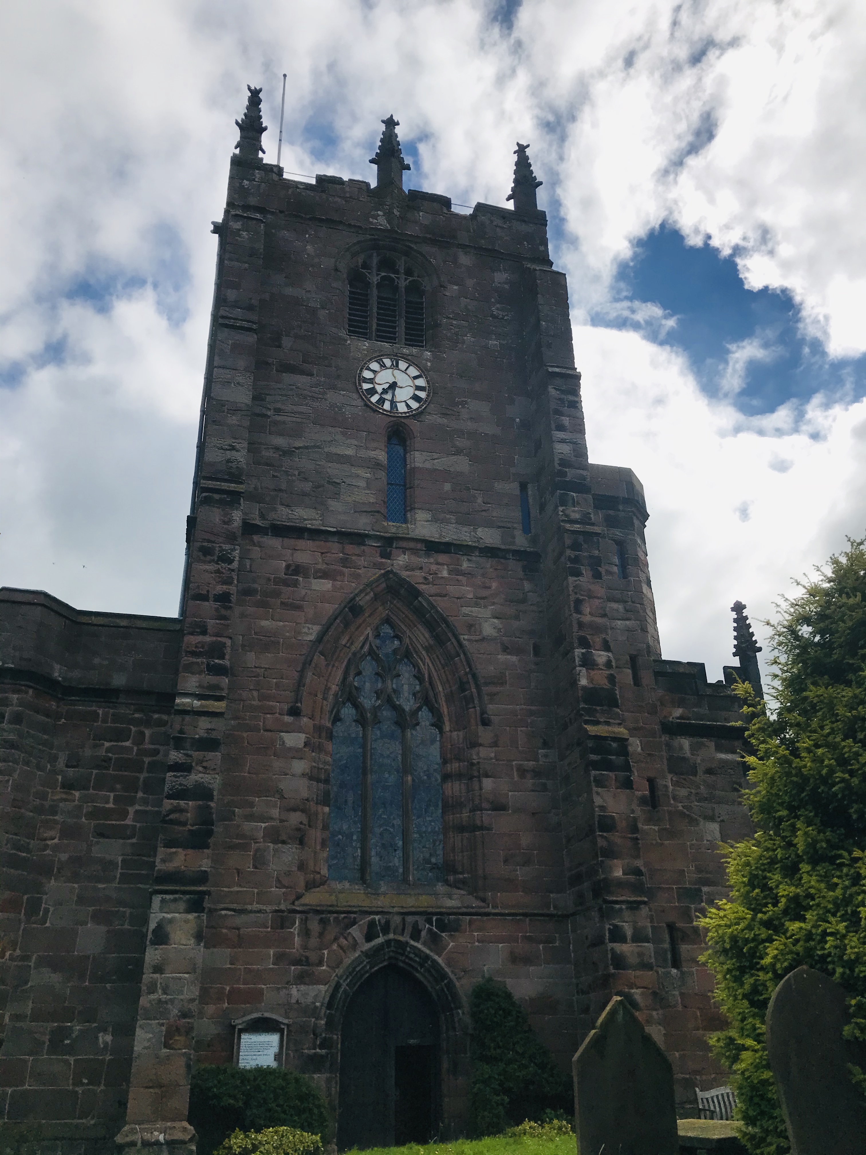 A sandstone church tower, with a clock face and stained glass window
