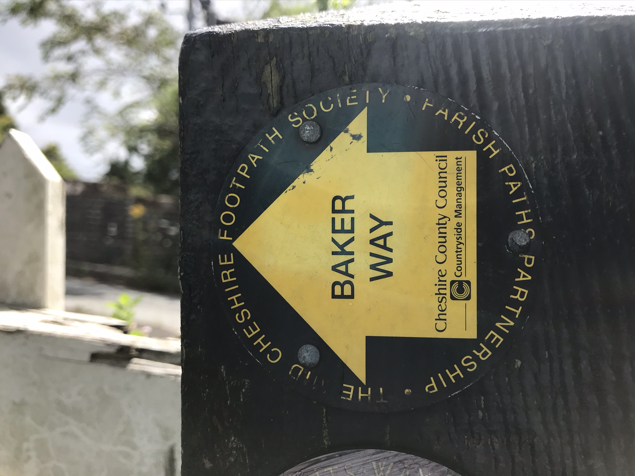 A close up of a yellow footpath sign with the words "Baker Way" on a wooden post