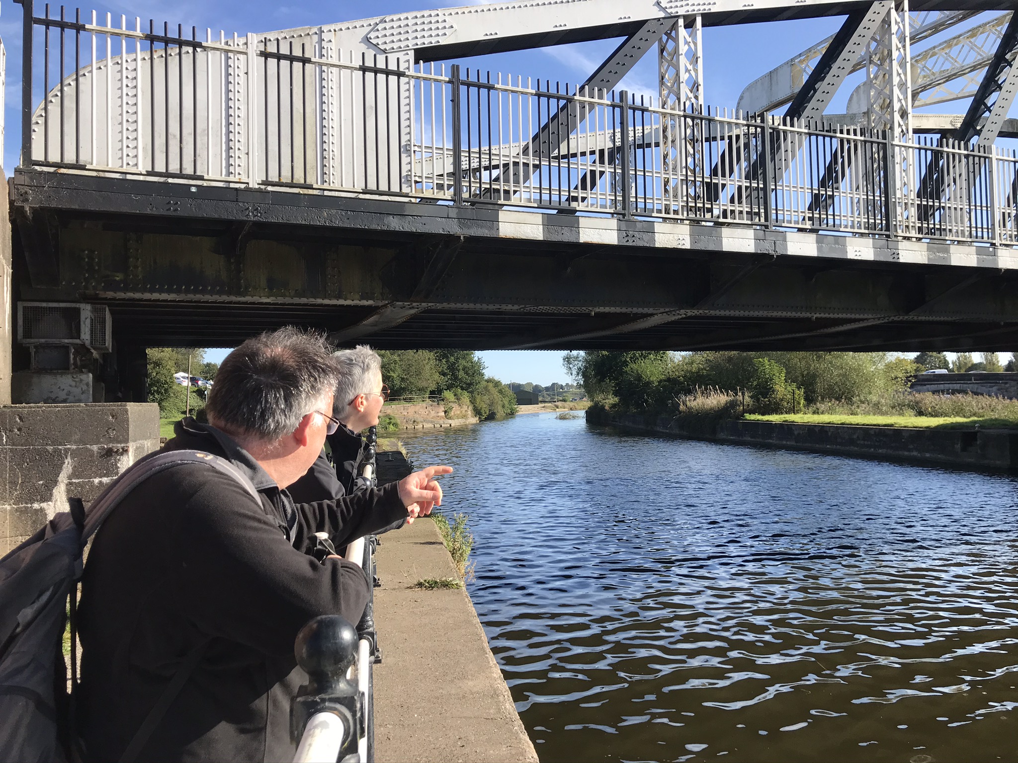 Two people leaning on railings looking at a steel bridge overhead