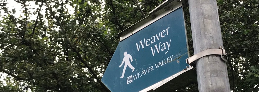 A green footpath sign against a leafy hedge