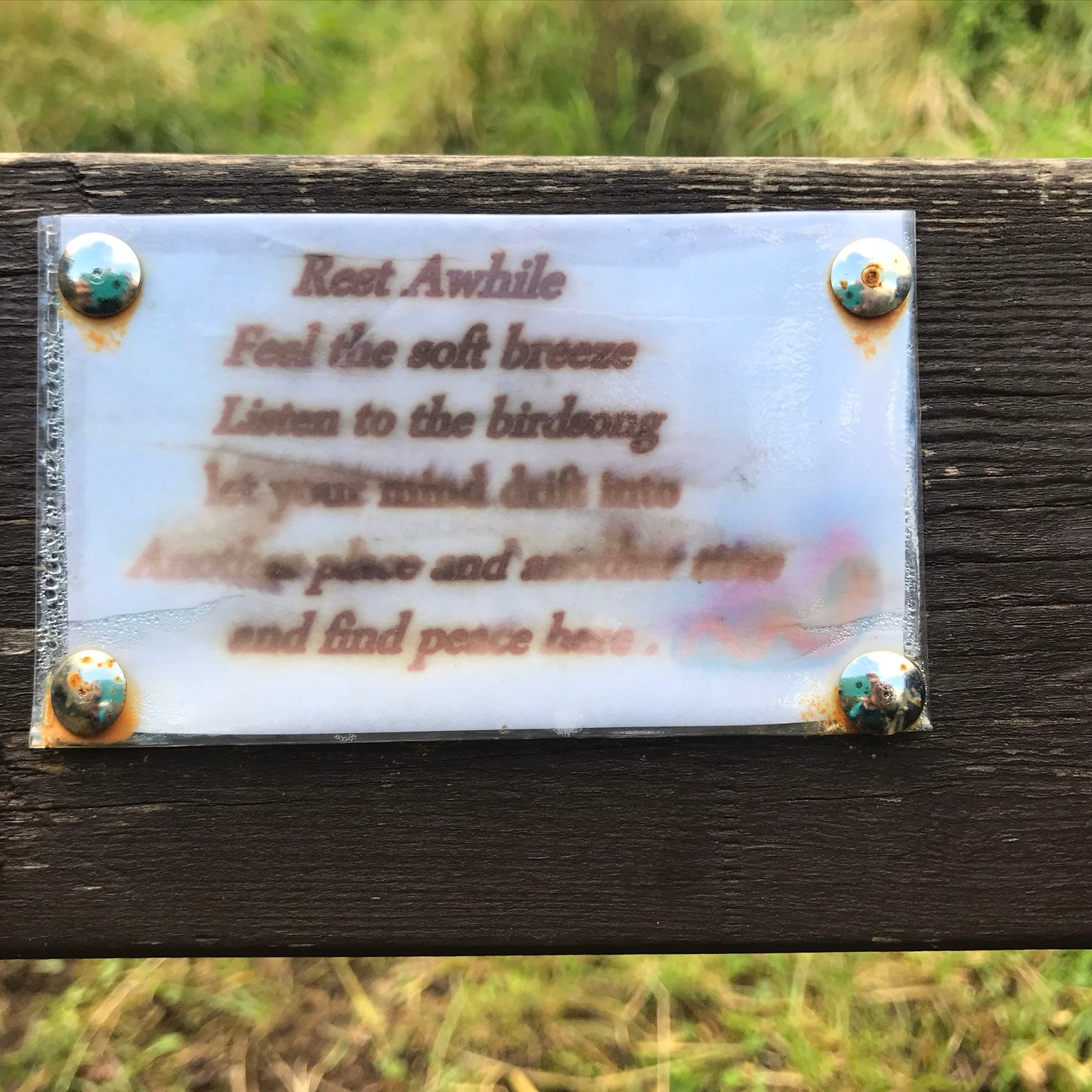 A paper sign, the ink blurred by water, in a plastic envelope pinned to wood with rusty drawing pins