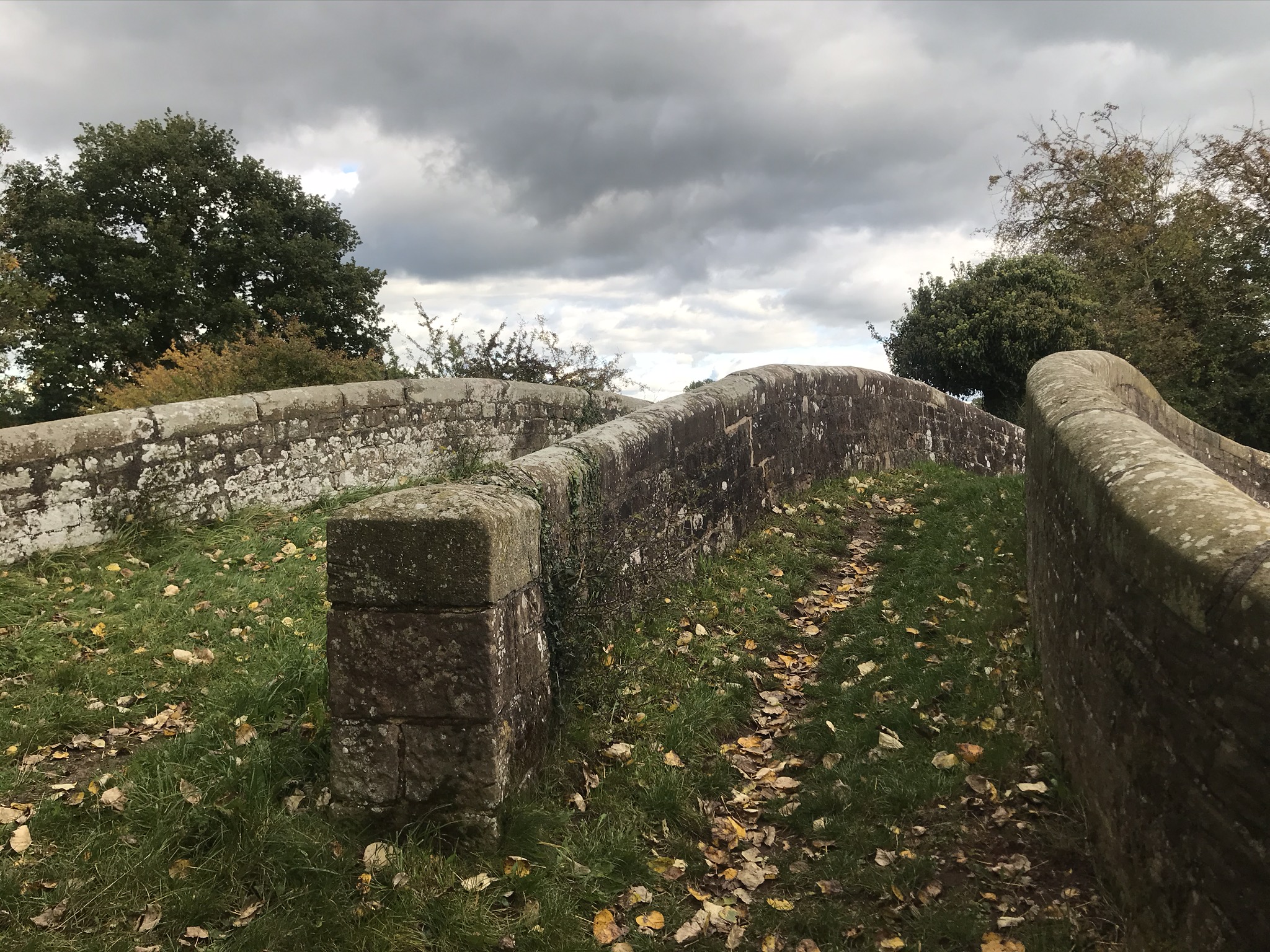 A view from the end of a canal bridge, there is a stone wall dividing the path on the bridge into two paths.
