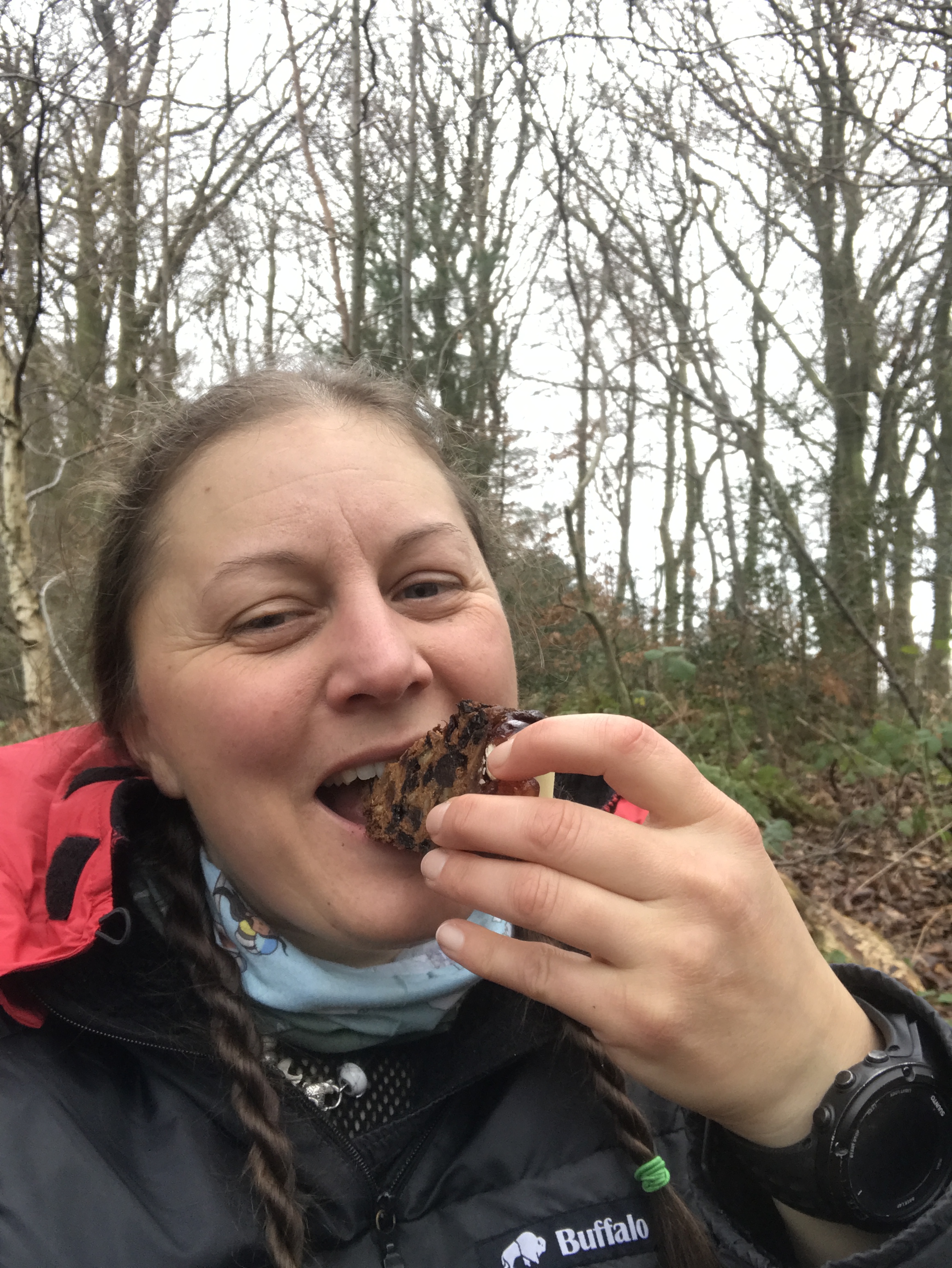A selfie of me eating fruit cake, in the background are bare trees