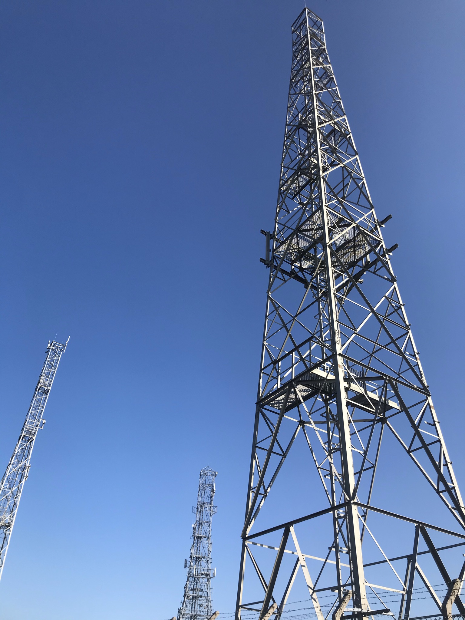 Looking up at three steel masts against a bright blue sky