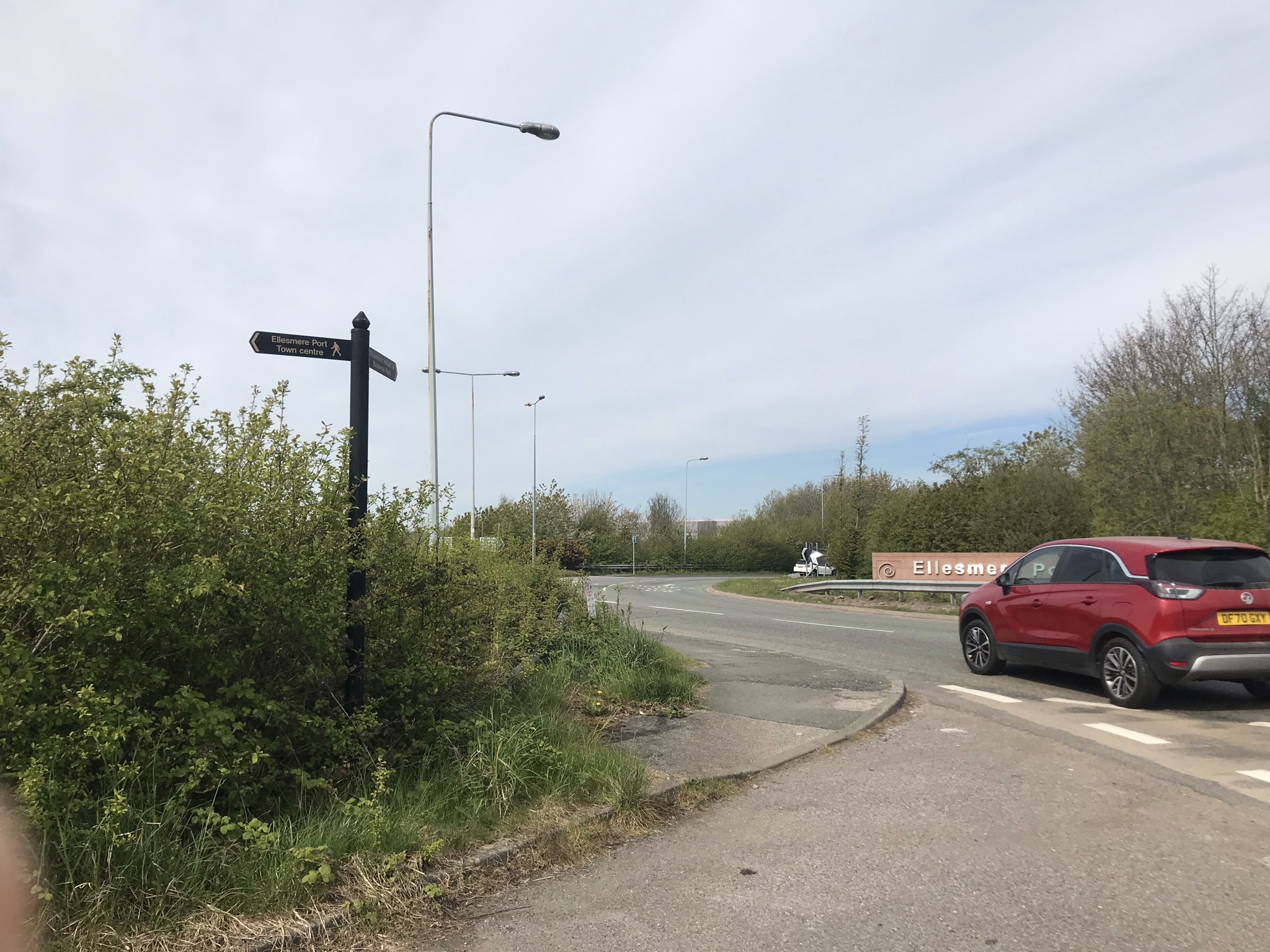 A black finger post for a footpath on a busy roundabout