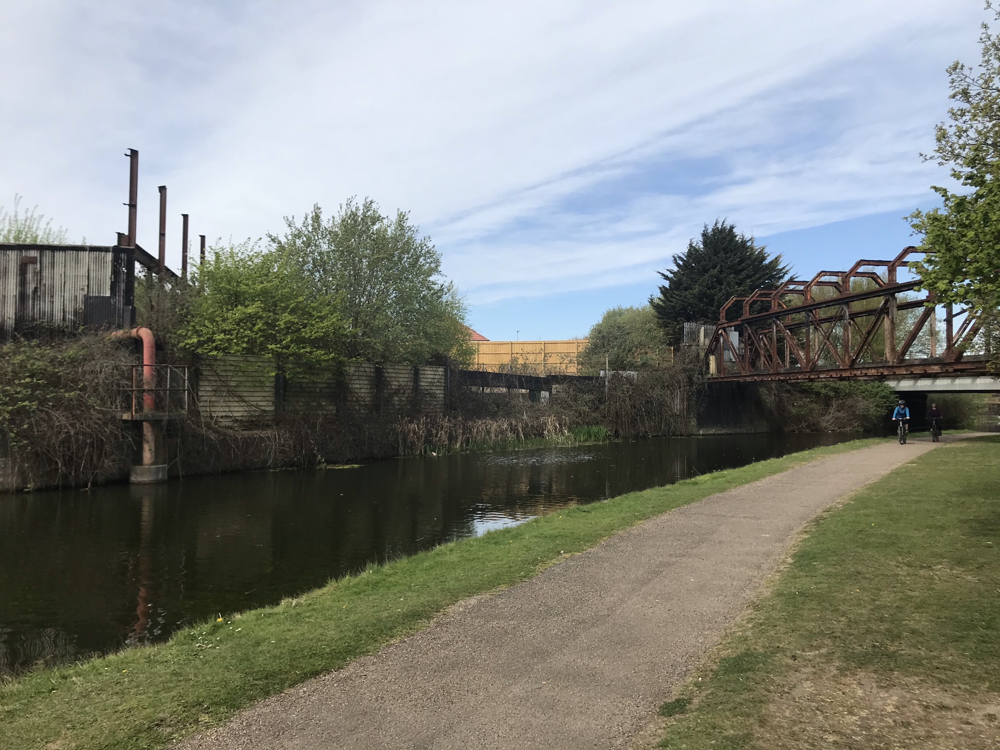 A towpath alongside the canal with a rusty steel frame bridge and dilapidated buildings