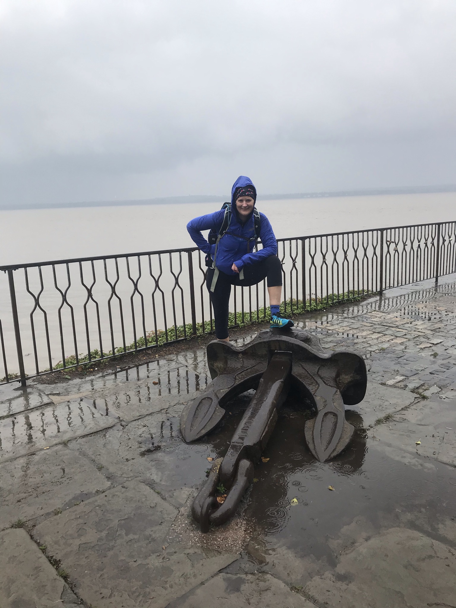 Sarah stands with one foot on an anchor. Behind her the sky is grey and rainy