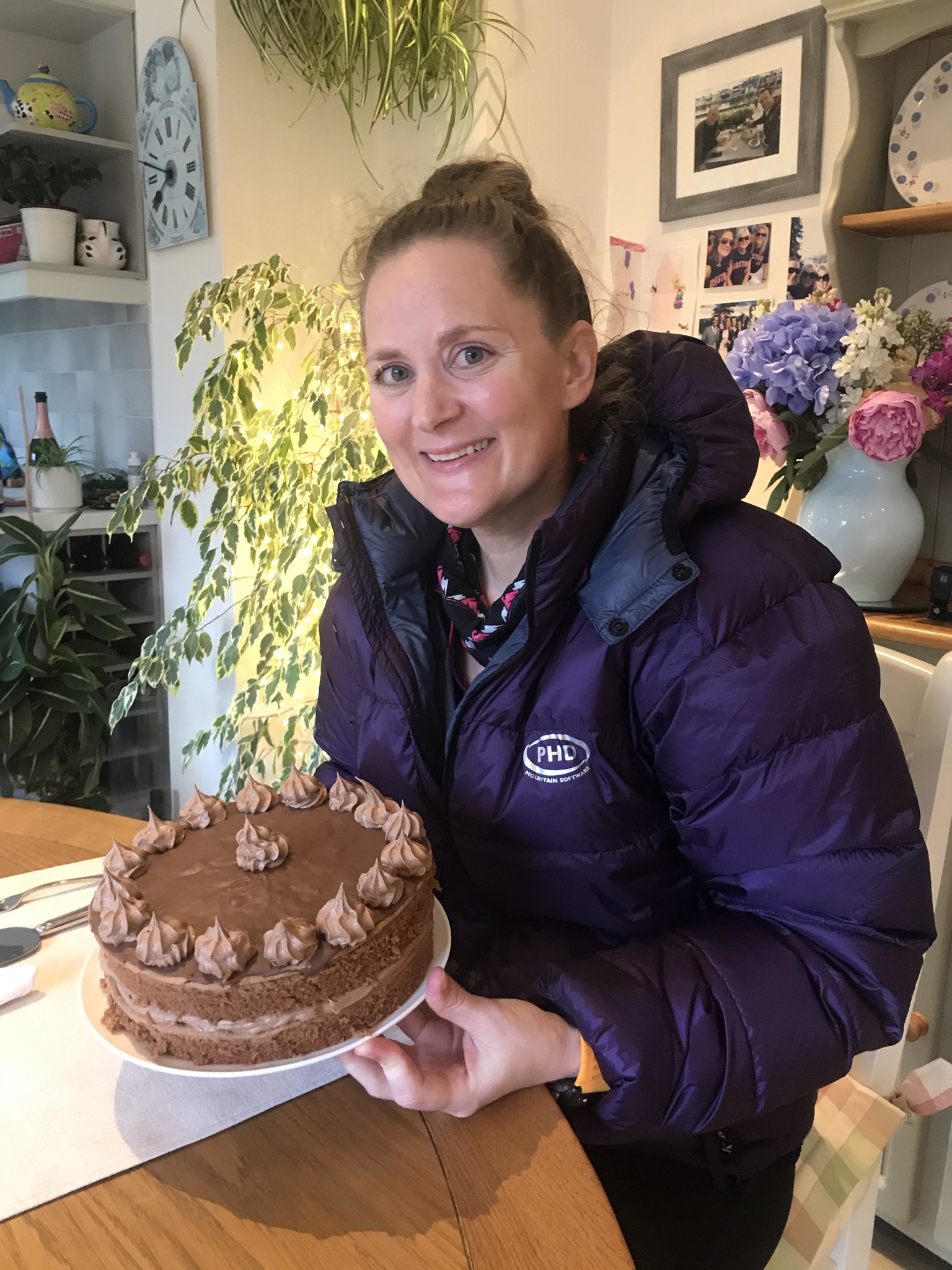 Sarah smiles at the camera holding a decorated chocolate cake