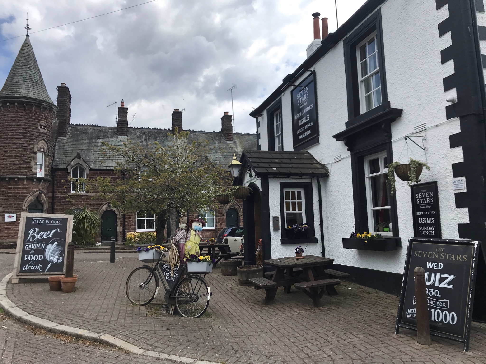 A black and white pub with two scarecrows on a bike outside.