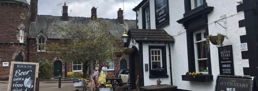 A black and white pub with two scarecrows on a bike outside.