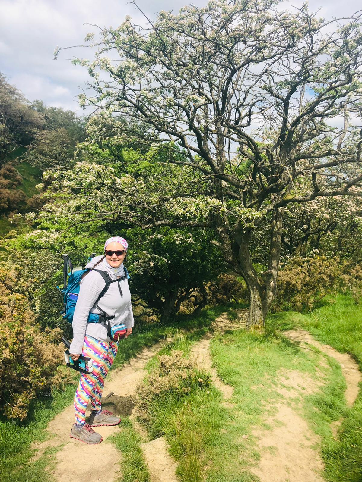 Ellen stands sideways smiling at the camera. Dusty paths lead off between trees in a narrow gorge.
