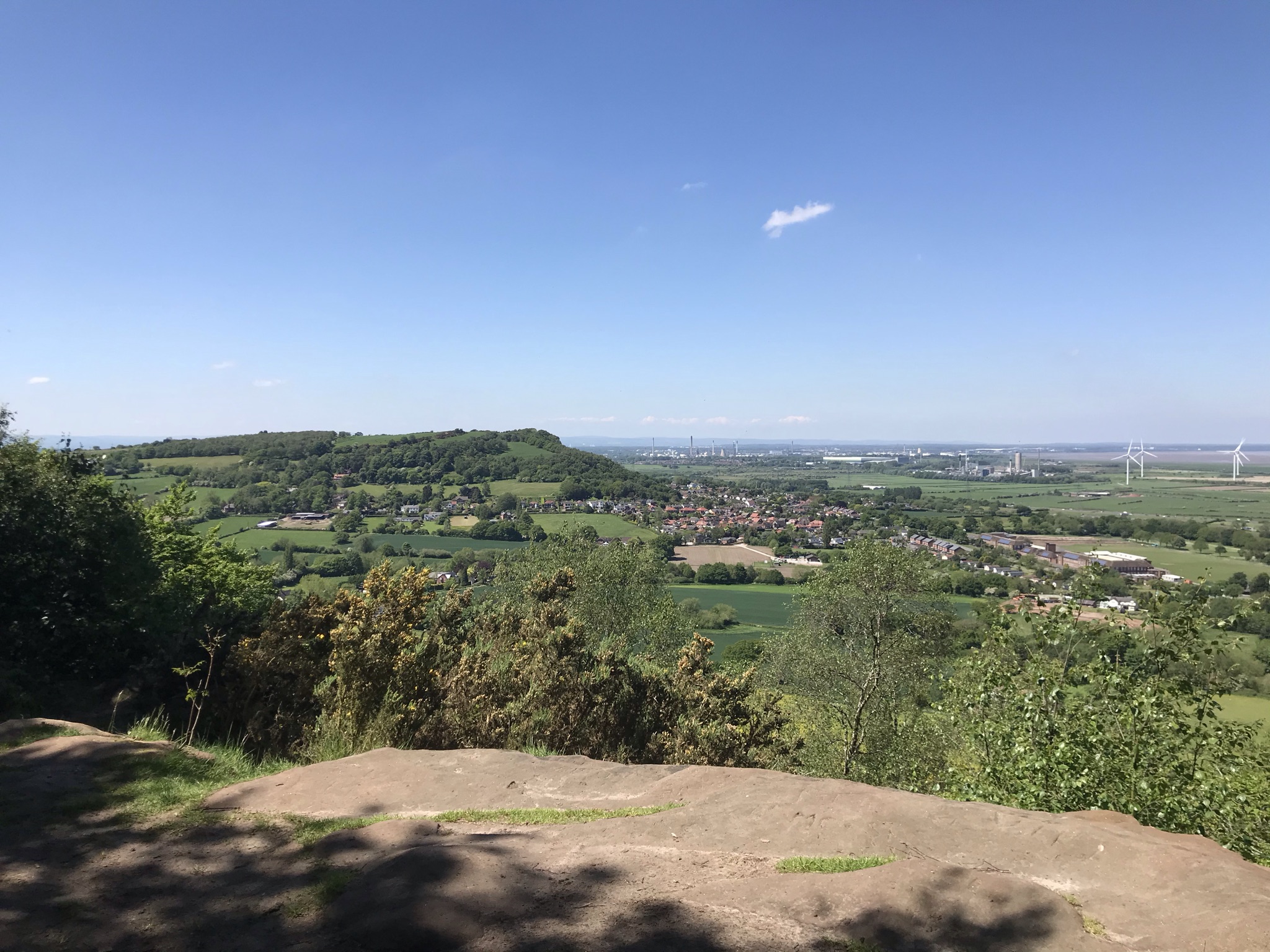 A rock ledge about the trees looing to the wooded Helsby Hill. There are wind turbines and one tiny cloud