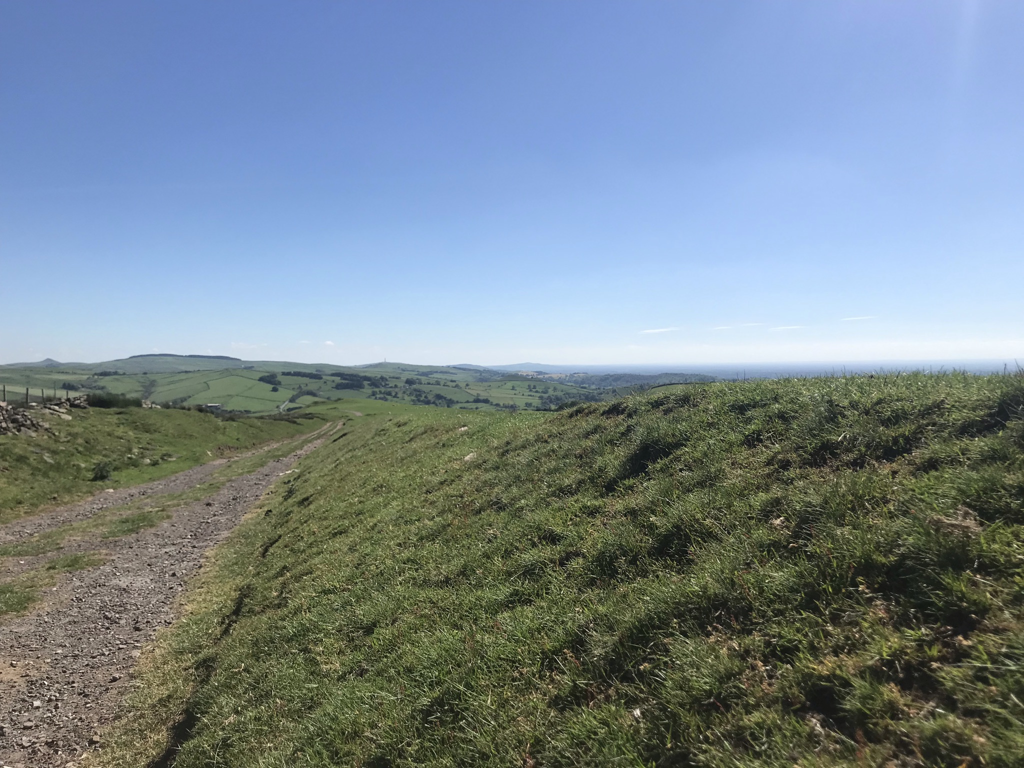 Clear blue sky above a stony track heading gently down hill between soft grassy banks. Hill can be seen on the horizon