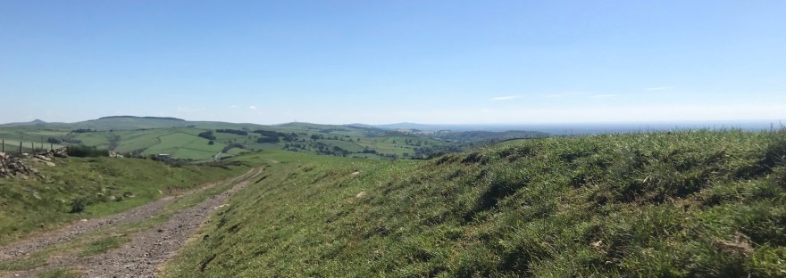 Clear blue sky above a stony track heading gently down hill between soft grassy banks. Hill can be seen on the horizon