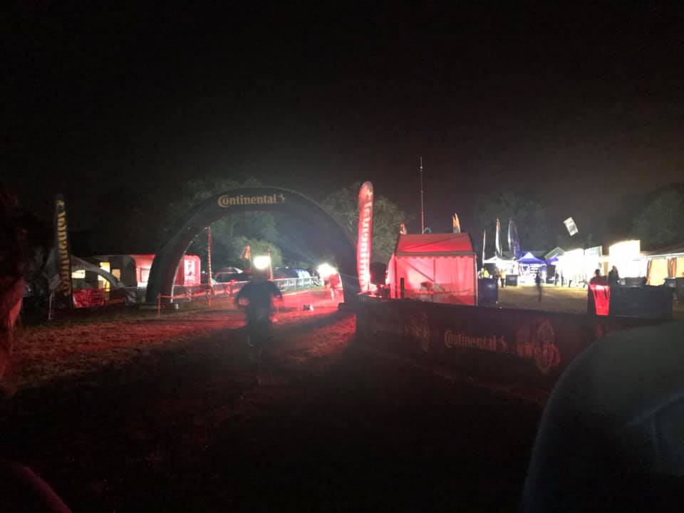A blurry picture of a runner wearing a headtorch. The have just run underneath a flood lit arch.