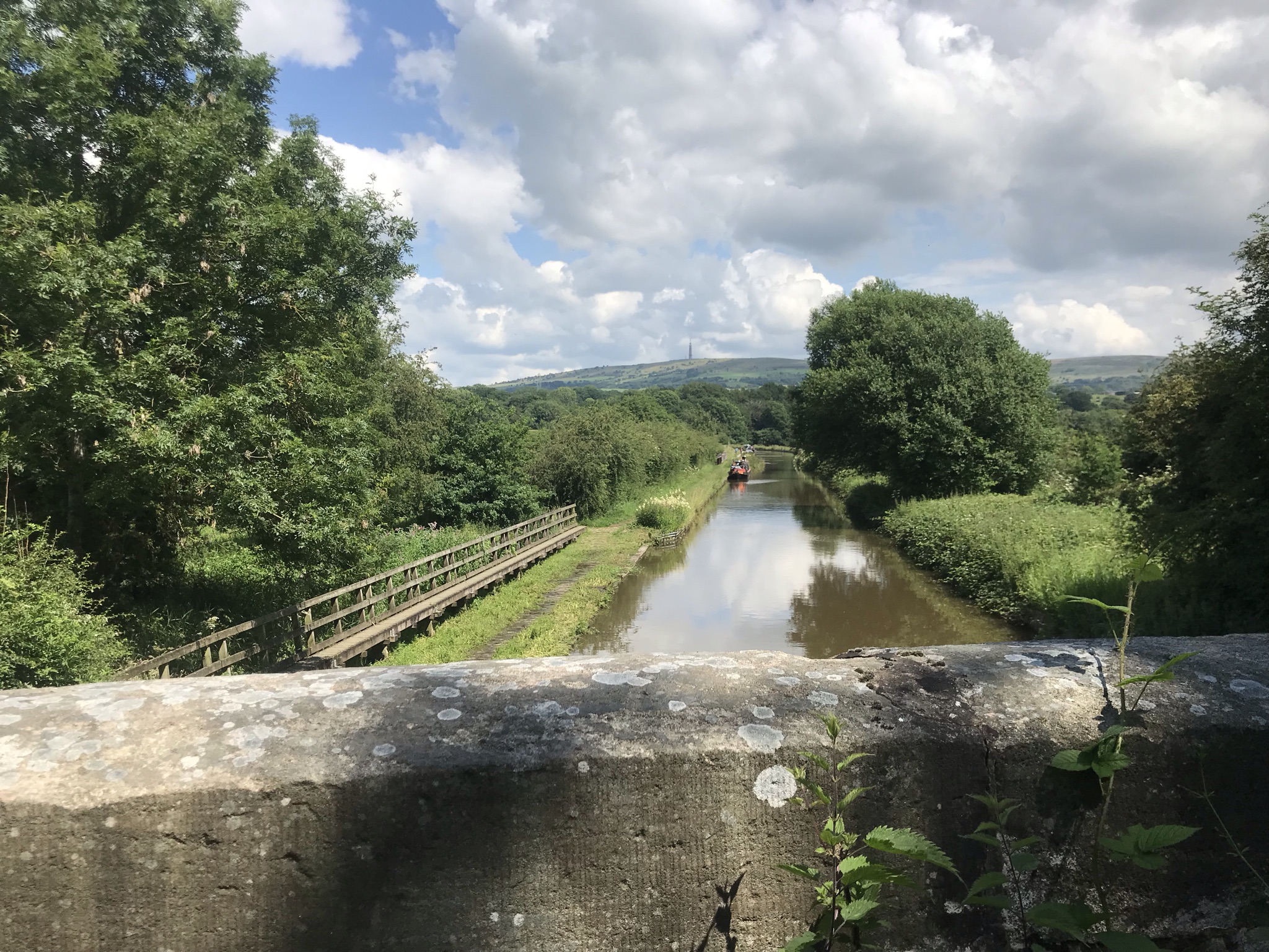 A distant hill with a solid radio mast is seen from a bridge over the canal