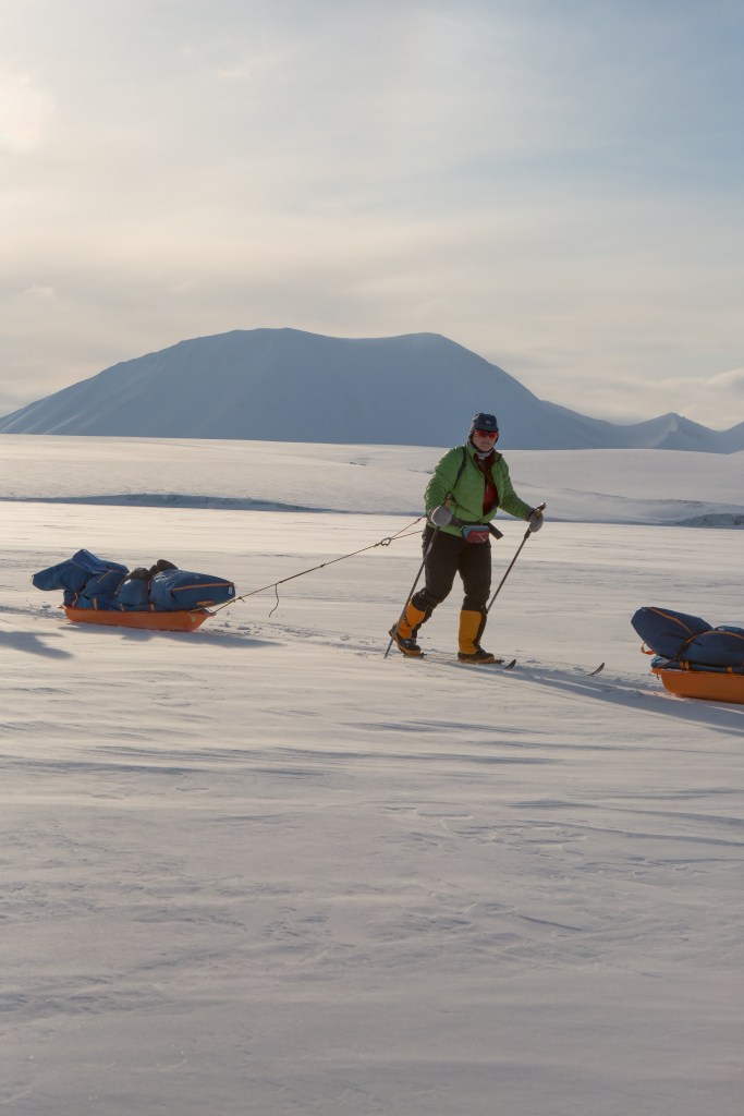 Me skiing pulling my pulk, in the distance is a snow covered mountain