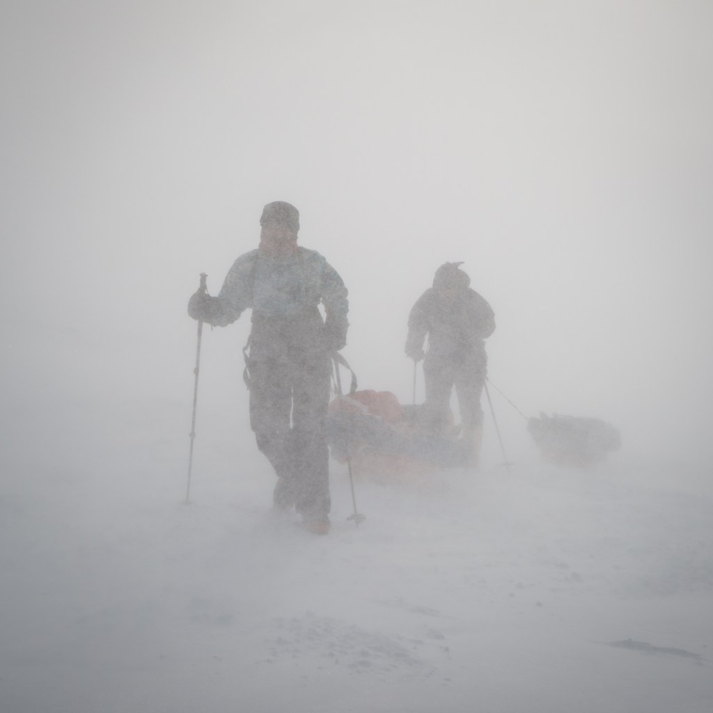 Me and a tent buddy pulling our pulks as we walk. The spindrift has blurred us to shadows.