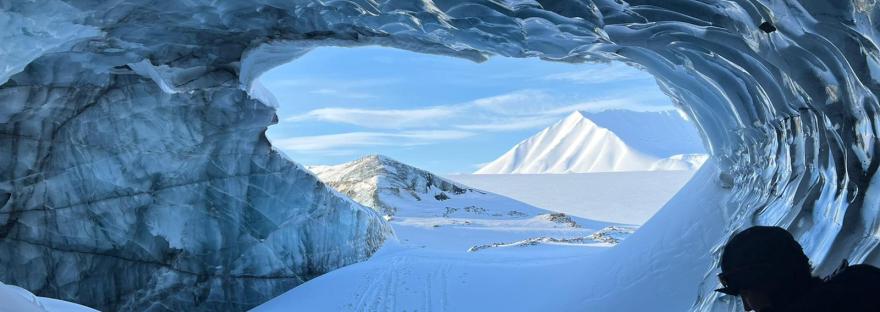 The view from inside the ice cave. On the ceiling, the ice looks polished reflecting the low light. Ski tracks and abandoned skis are in the entrance.