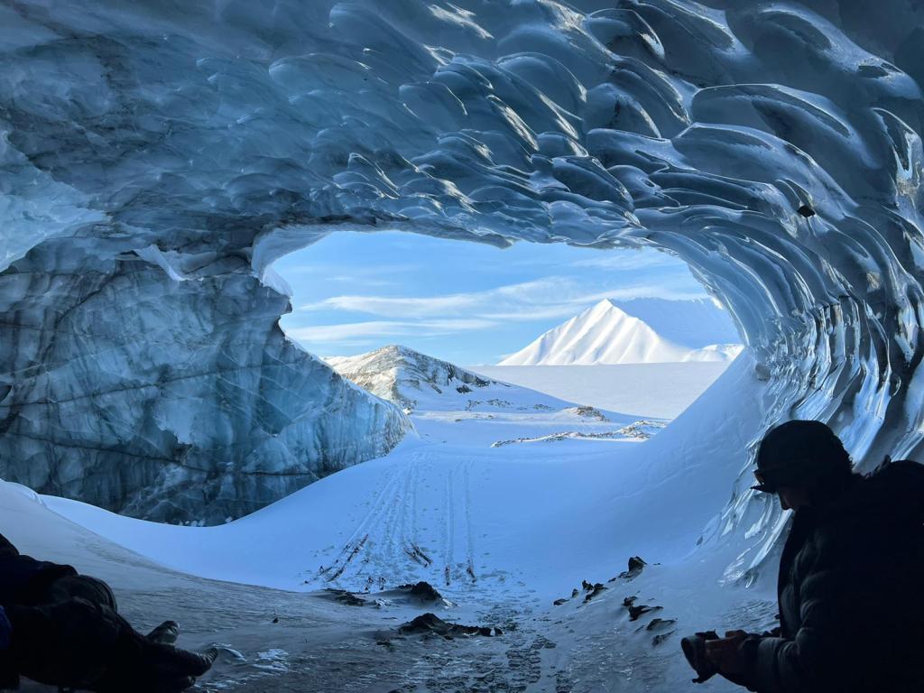 The view from inside the ice cave. On the ceiling, the ice looks polished reflecting the low light. Ski tracks and abandoned skis are in the entrance.
