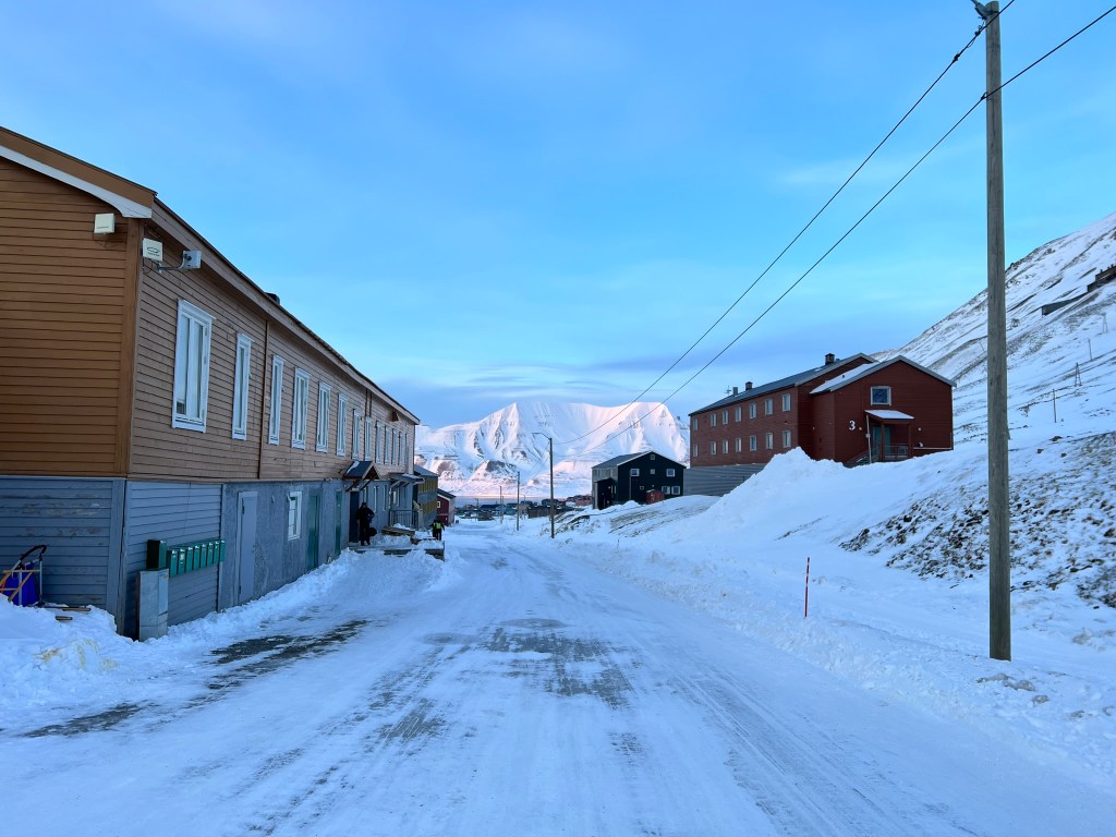 An view down the snowy street in Nybyen.  On the other side of the distant fjord is a snow covered mountain